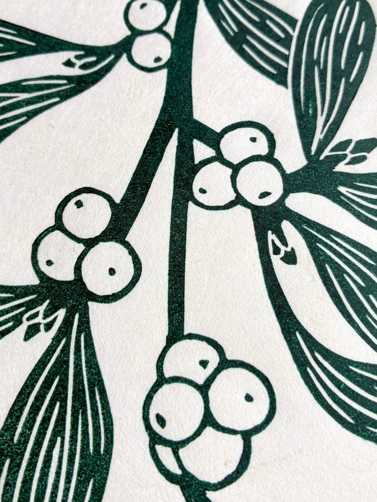 A close-up of a botanical print featuring dark green mistletoe branches with clusters of round berries and textured leaves on an off-white background.