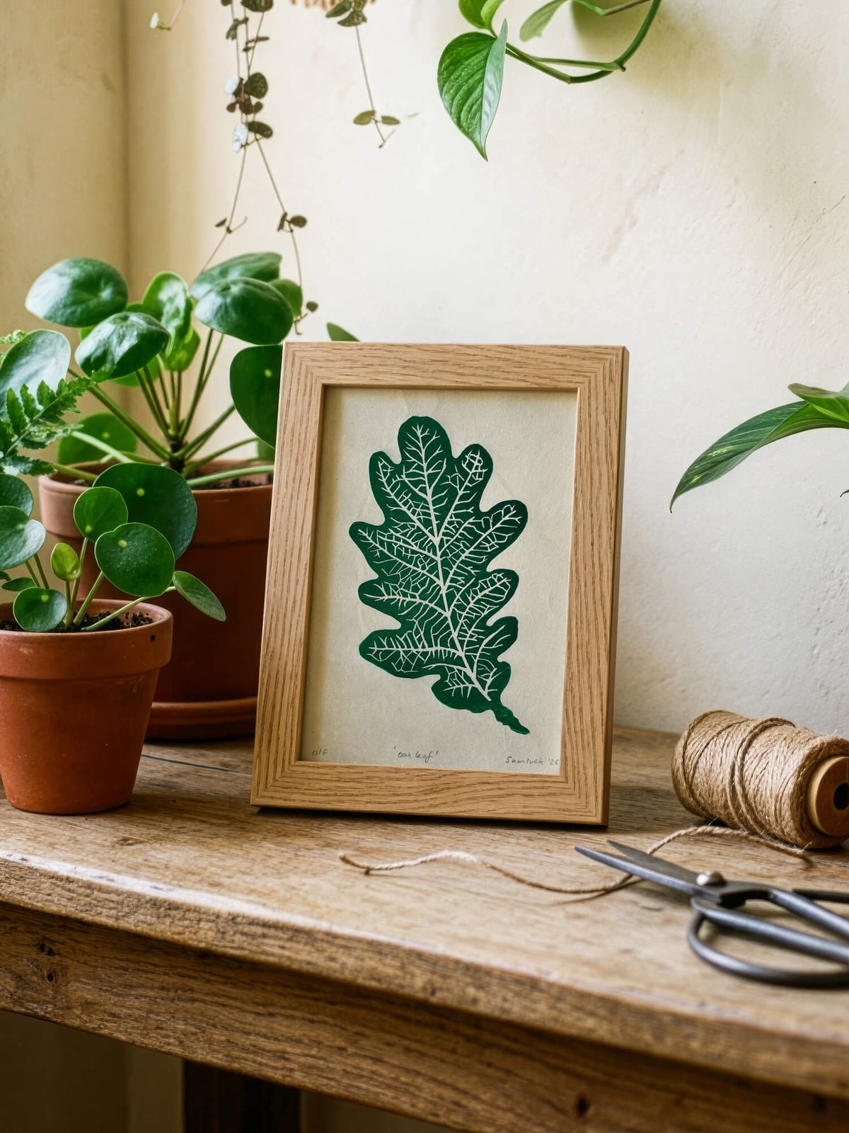 Small handmade oak leaf print in a wooden frame, on a gardening bench, with scissors and twine.