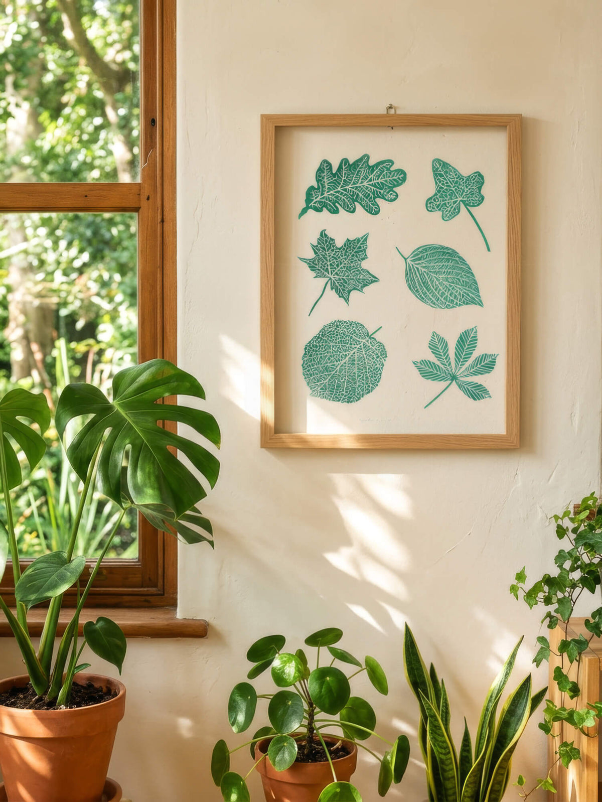 A picture frame containing botanical leaf wall art, hanging in a cosy interior surrounded by plants.