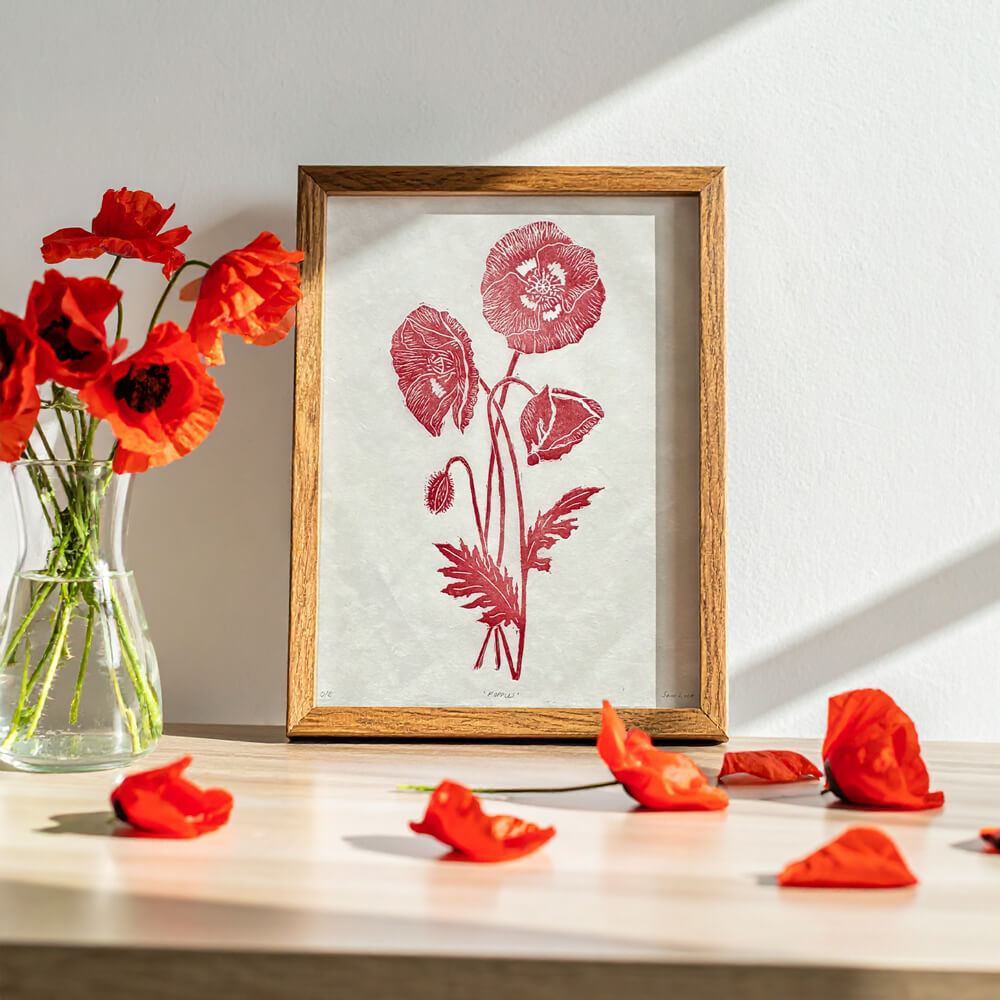 Framed botanical artwork of red poppies next to a vase of wild poppies. Sam Luck 8 x 10 inch linocut print wall art, UK.