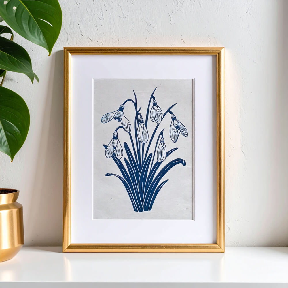 Framed botanical artwork of snowdrops next to a monstera plant. Sam Luck 8 x 10 inch linocut print wall art, UK.