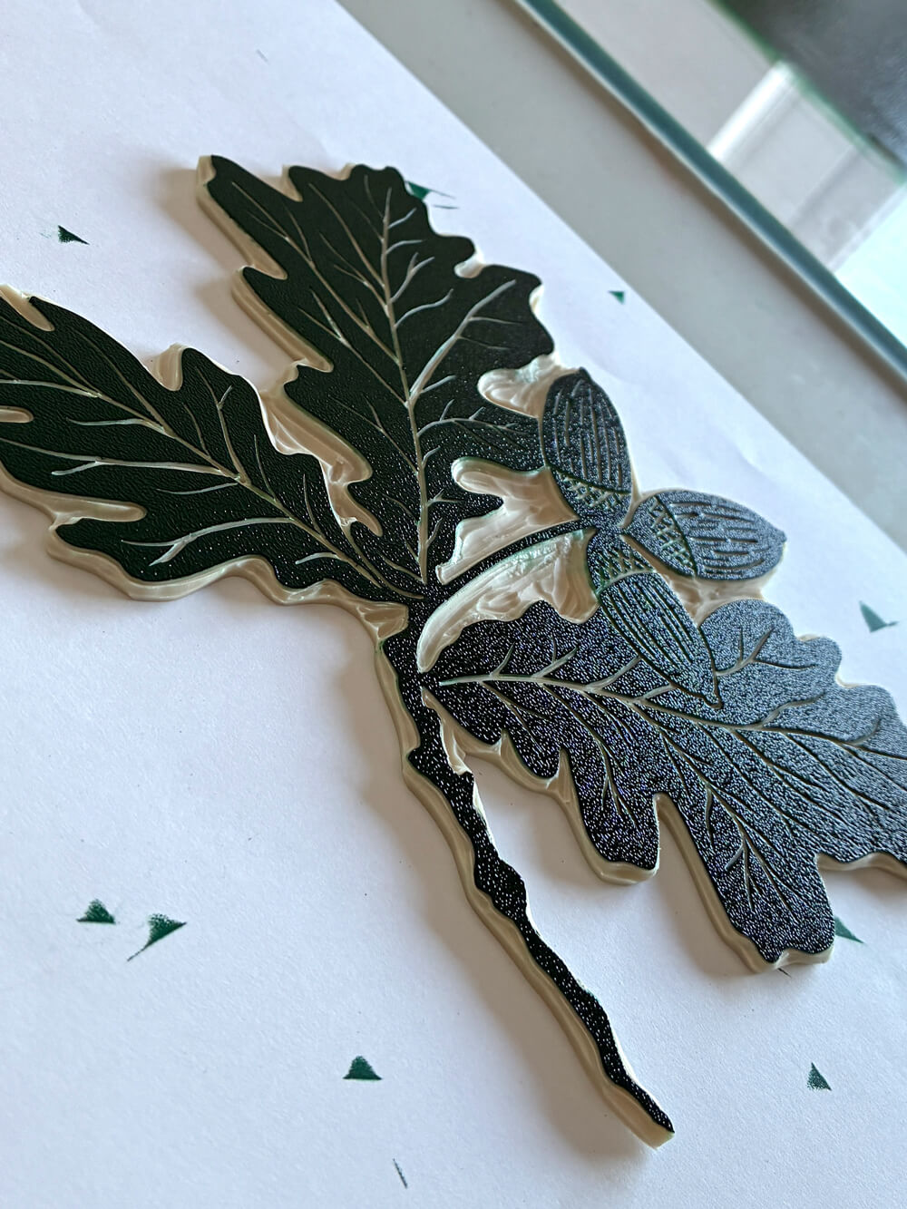 Linocut block of an acorn leaf, covered in green ink.