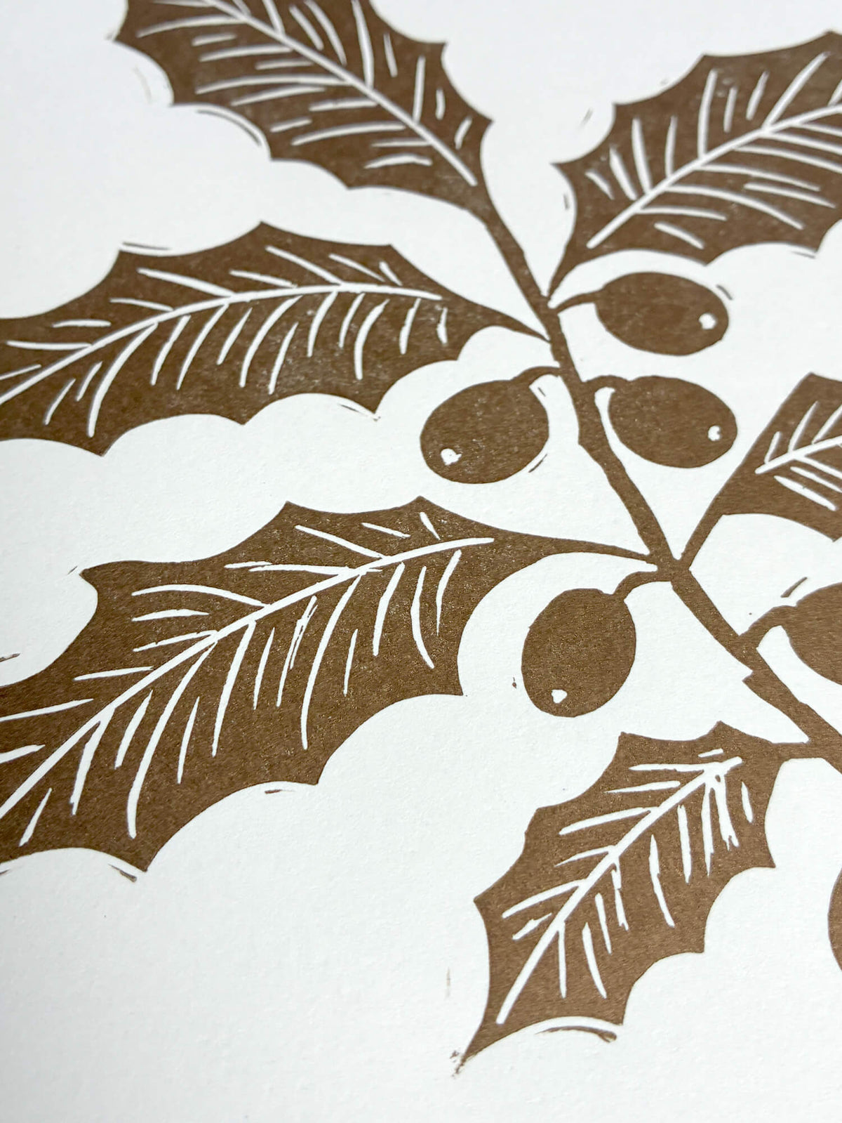 A close-up of a gold holly leaf and berry print on a handmade linocut Christmas card.