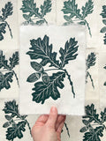 Handmade oak leaf and acorns linocut print on handmade paper, held by hand, full view from above hand printed by UK botanical linocut artist Sam Luck.