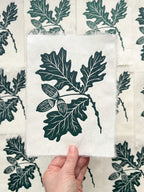 Handmade oak leaf and acorns linocut print on handmade paper, held by hand, full view from above hand printed by UK botanical linocut artist Sam Luck.