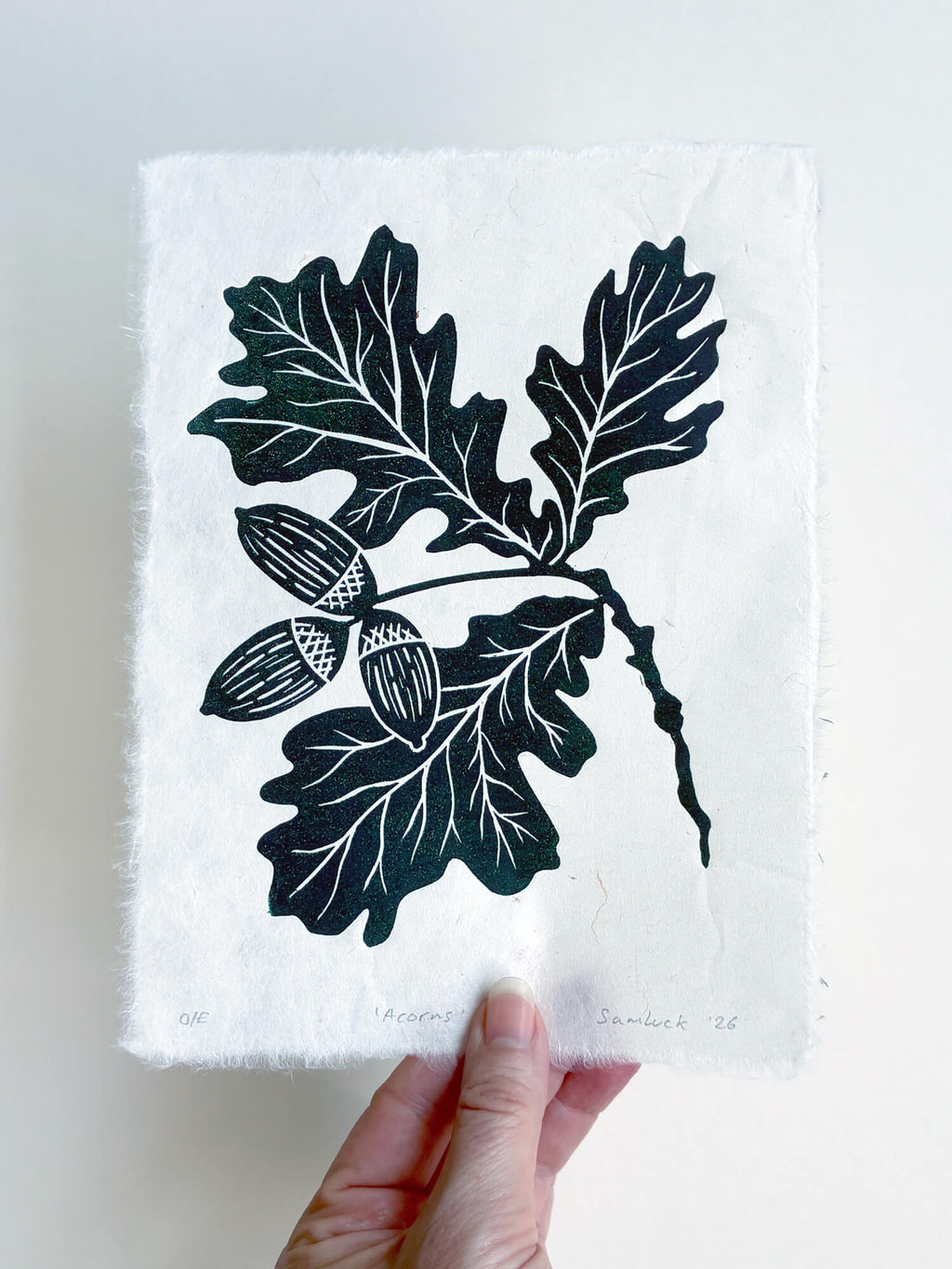 Hand holding a green acorn and oak leaf linocut print, handmade wall art, UK.