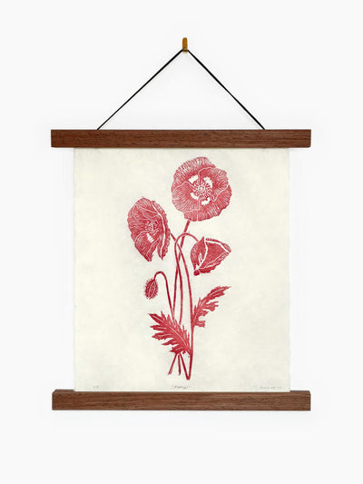 A hanging wall art print featuring a red botanical illustration of wild poppies on an off-white textured background in a wooden hanging frame.