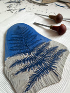 Detail of linocut carving on a grey linoleum block with two carving tools. 