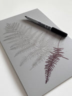 Drawing of a fern leaf on a battleship grey lino block using a sharpie pen. Created by Sam Luck, Hampshire based linocut artist.