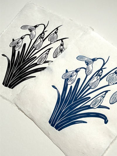 Handmade snowdrops linocut prints on handmade paper in black and blue ink, side view on white background, hand printed by UK linocut artist Sam Luck