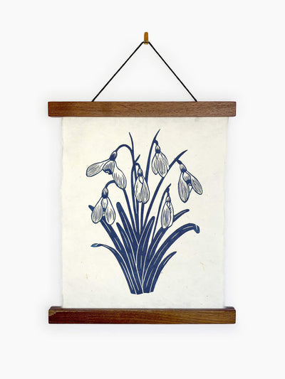Image of a linocut print of snowdrop flowers in a poster frame hanging on a white wall.