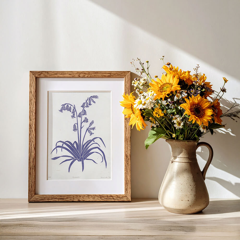 Framed print of English bluebells next to a vase of British wildflowers.