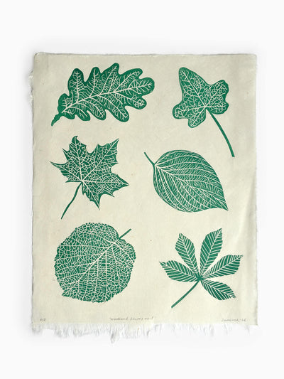 A hand crafted linocut print featuring a green botanical print of six different leaf types, on handmade paper, laid flat against a white background.